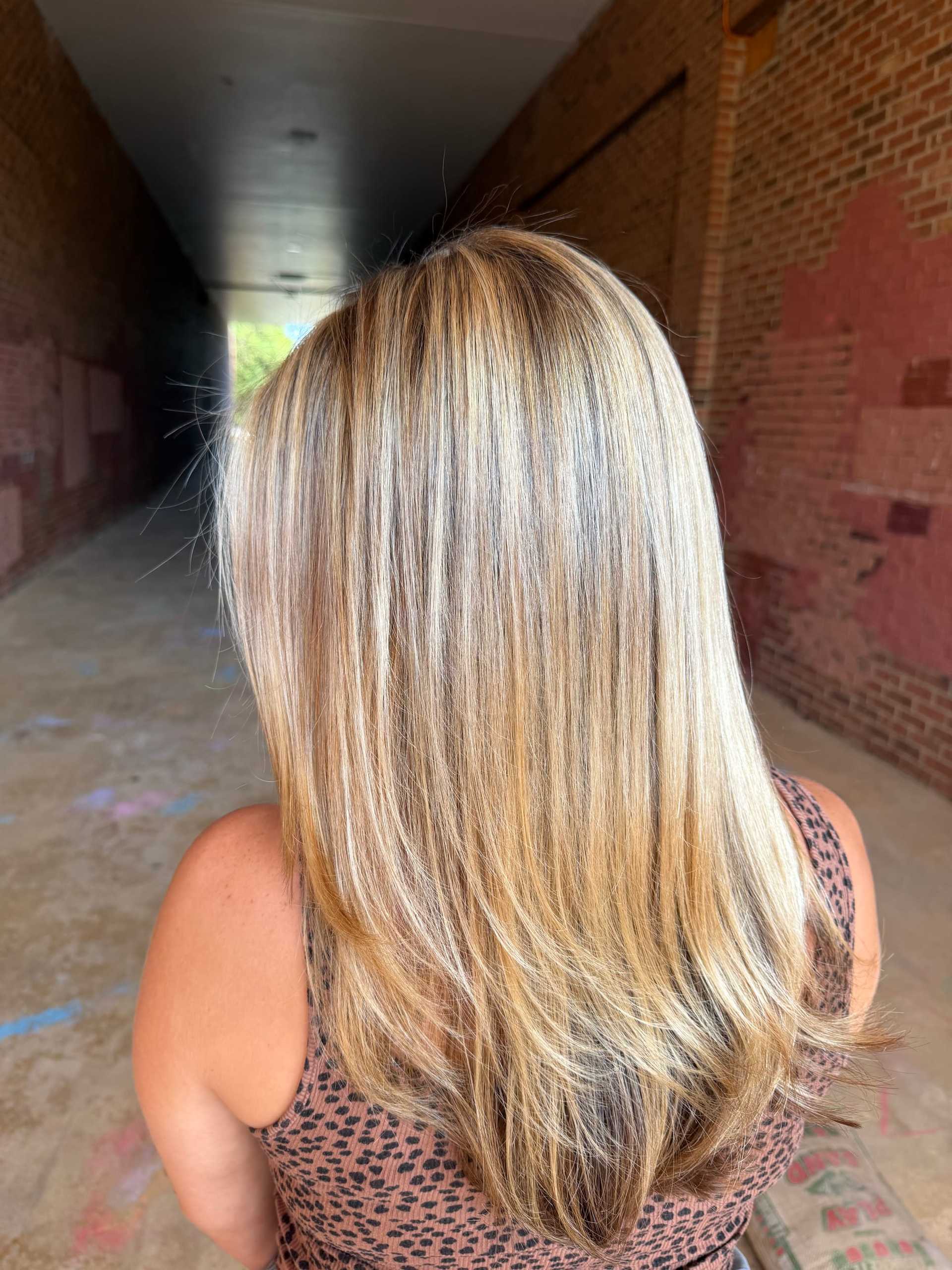 Blonde hair with highlights, viewed from the back, in a brick-lined walkway.