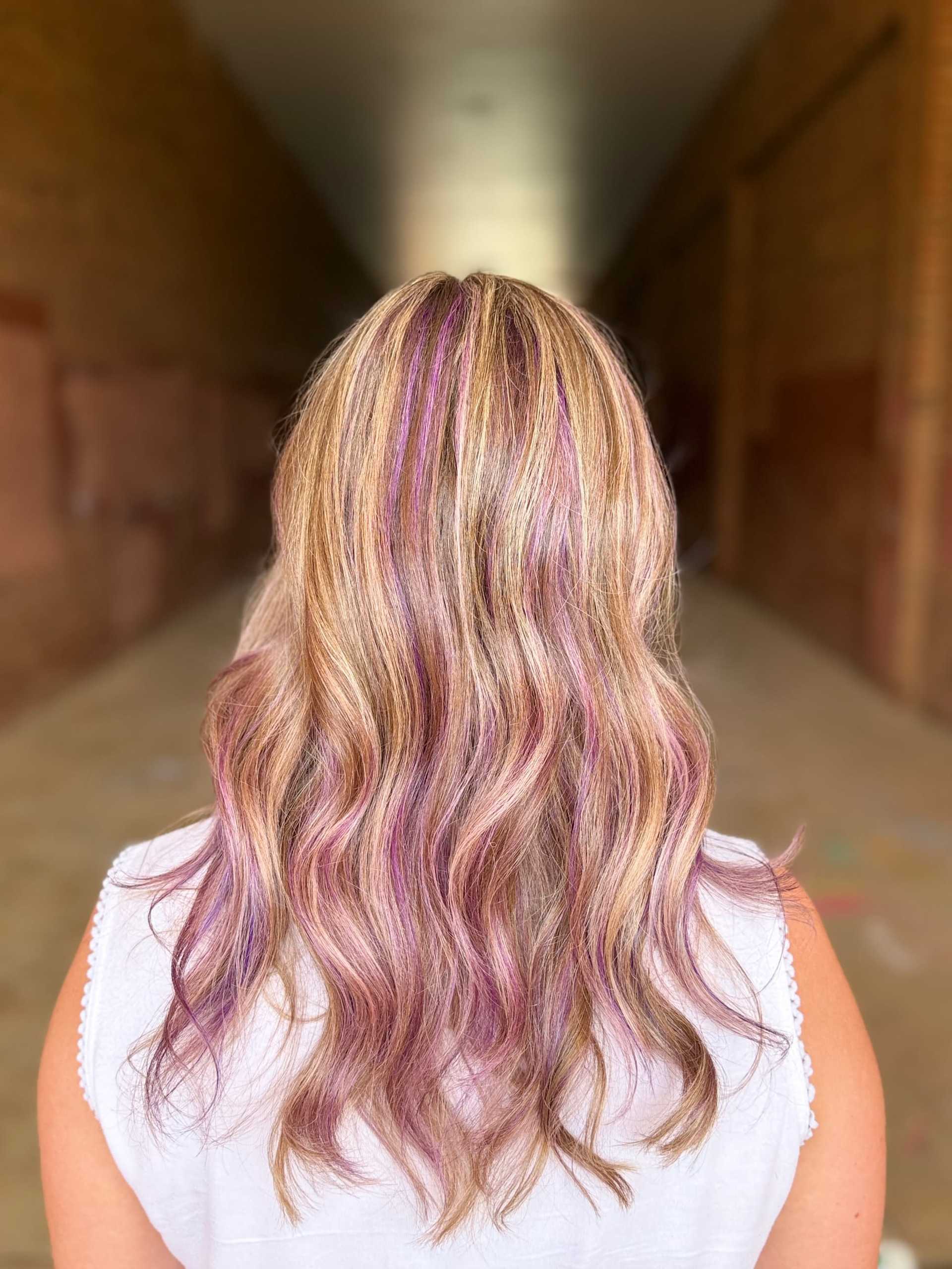 Blonde hair with pink highlights viewed from the back in a corridor.