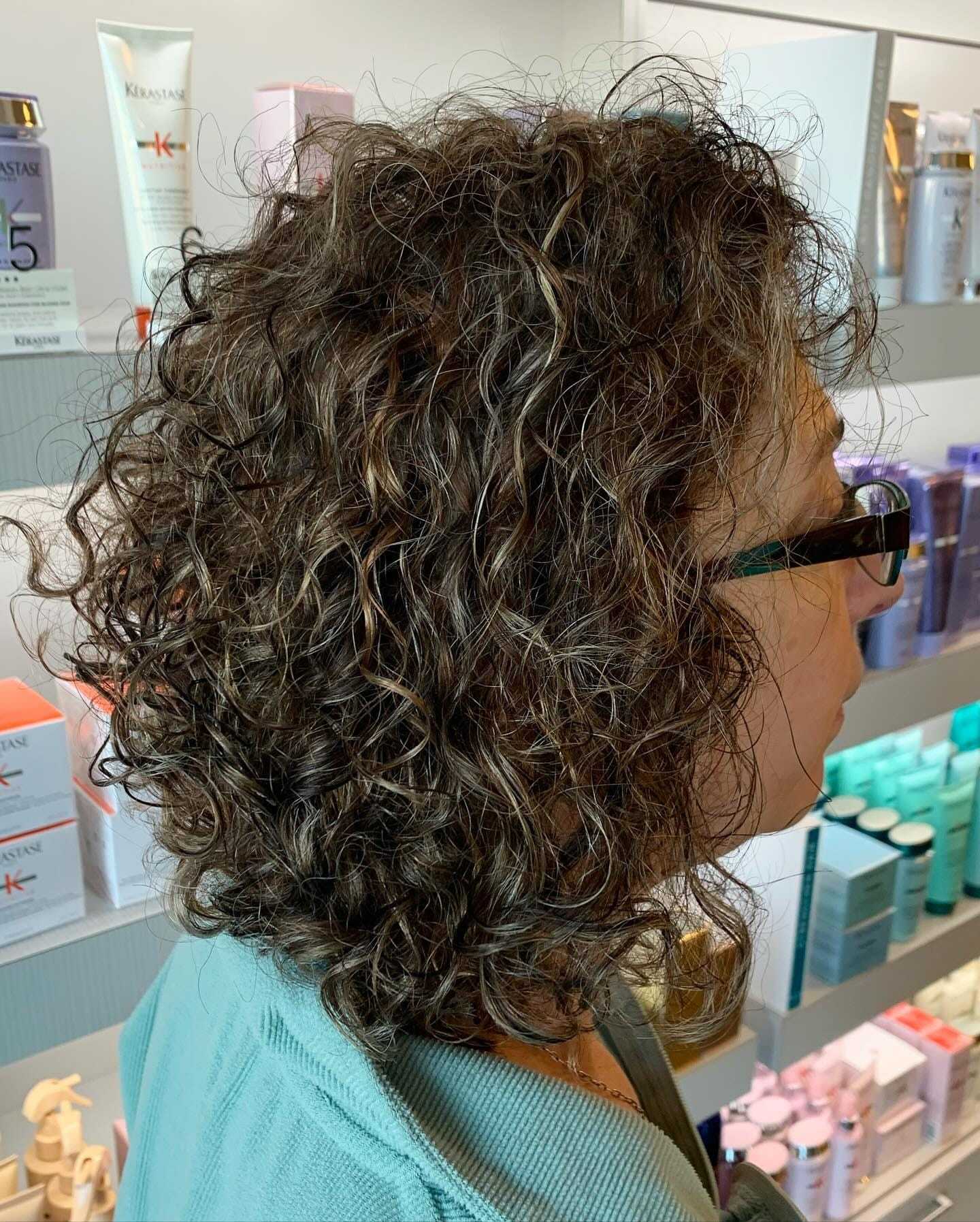 Side profile of a person with curly hair in a salon surrounded by hair products.